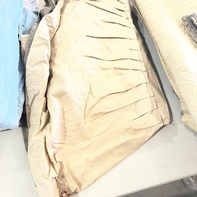 Sale Photo Thumbnail #124: Folded beige pleated window curtain panel alongside assorted bedding and linens.