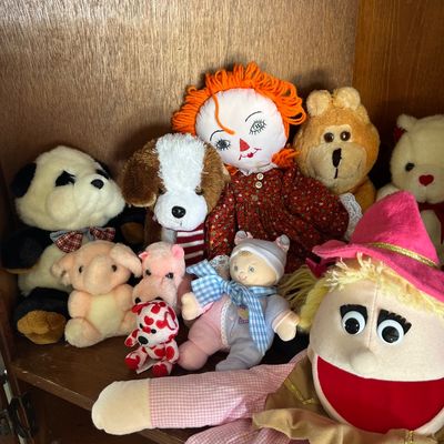Sale Photo Thumbnail #46: Collection of assorted vintage plush toys and hand puppets, including a Raggedy Ann doll, stuffed animals, and a witch puppet, arranged on a wooden cabinet shelf.