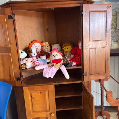 Sale Photo Thumbnail #48: Large wooden corner armoire cabinet with bi-fold doors, currently filled with an assortment of vintage plush stuffed animals and dolls.