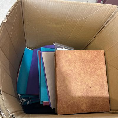 Sale Photo Thumbnail #65: Cardboard box filled with assorted office supplies, including colorful paper folders, cardstock, and a tan binder.