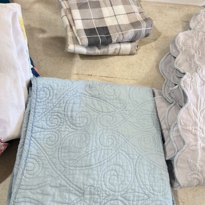 Sale Photo Thumbnail #118: Folded light blue quilted throw blanket featuring a scroll stitching pattern alongside other neatly folded household linens.