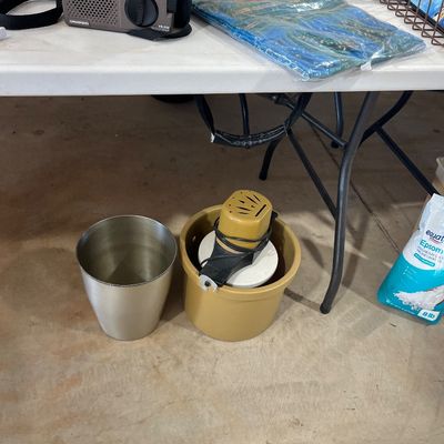 Sale Photo Thumbnail #101: Vintage electric ice cream maker sitting under a table alongside a stainless steel bucket, Grundig portable radio, and packaged household goods.