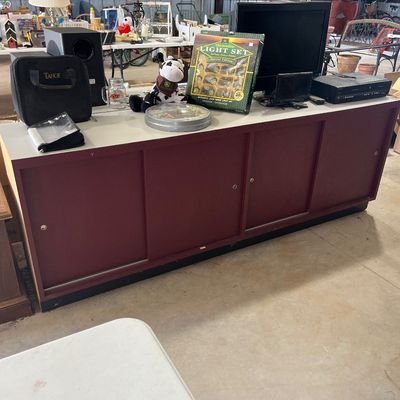 Sale Photo Thumbnail #111: Long maroon credenza with sliding cabinet doors topped with various household electronics, decor, and collectibles.
