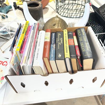 Sale Photo Thumbnail #99: Cardboard produce box packed with various hardcover and paperback books, surrounded by eclectic household items.