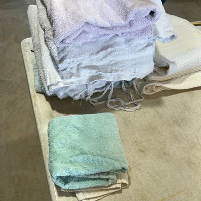 Sale Photo Thumbnail #119: Stack of assorted bath towels, washcloths, and linens on a folding table, showing wear and fraying on some edges.