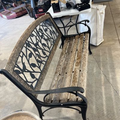 Sale Photo Thumbnail #125: Outdoor garden bench featuring black cast metal armrests and back insert with a leaf motif, complemented by weathered wood slats.