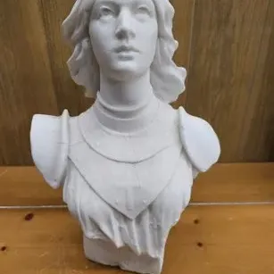 Classical-style white bust of Joan of Arc wearing armor, set against a wood panel background.