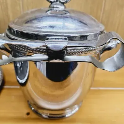 Vintage silver-plated ice bucket with a fitted lid and matching ice tongs attached.