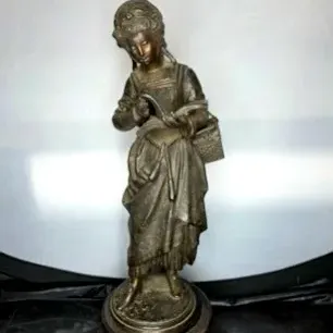 Antique bronze or metal sculpture of a young reading woman with a basket, mounted on a round wooden base.