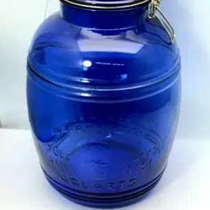 Cobalt blue glass barrel-shaped jar featuring embossed lettering and a wire bale flip-top lid with a rubber seal.