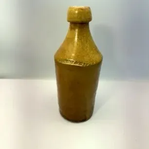 Antique stoneware ginger beer bottle featuring a tan and mustard yellow salt-glazed finish.