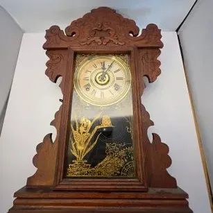 Antique carved oak gingerbread mantle clock featuring a decorative gold stenciled glass door panel and a brass dial with Roman numerals.