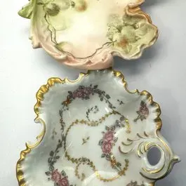 Pair of antique porcelain leaf-shaped dishes with scalloped, gilded edges and hand-painted floral motifs.