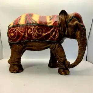 Vintage painted resin or composite elephant figurine, decorated in a traditional circus or ceremonial blanket with red, gold, and yellow...