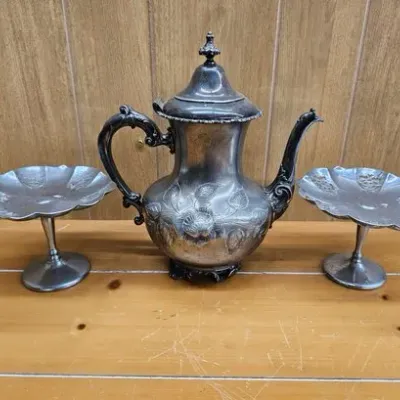 Vintage tarnished silver-plated coffee pot with floral engraving, flanked by a pair of matching scalloped pedestal candy dishes.