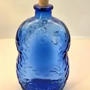 Vintage cobalt blue glass bottle with raised embossed botanical patterns and a cork stopper.