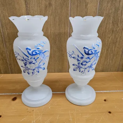 Pair of frosted white glass vases featuring hand-painted blue bird and floral motifs with ruffled, gold-trimmed rims.