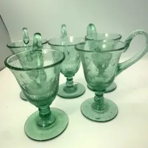 Set of five light green hand-blown glass punch or Irish coffee mugs featuring high looped handles and pedaled bases.