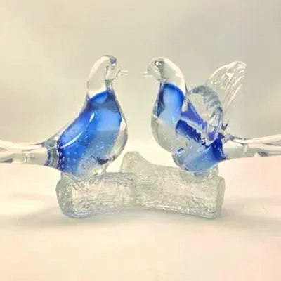 Hand-blown art glass sculpture featuring two blue and clear lovebirds perched on a frosted glass log base.