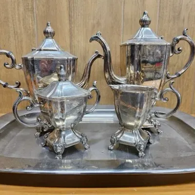 Vintage silver-plated tea and coffee service with matching tray, featuring ornate handles and urn-shaped finials.