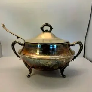 Vintage ornate silver-plated soup tureen with a fitted lid, decorative handles, footed base, and matching ladle.