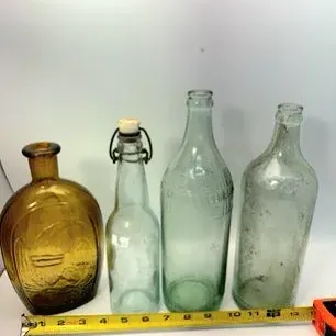 Collection of four vintage glass bottles, including an amber glass eagle flask and various clear and green tinted glass vessels.