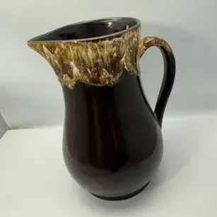 Vintage ceramic pitcher featuring a dark brown body with a mottled, cream-colored drip glaze rim and handle.