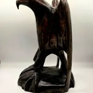 Hand-carved dark wood eagle figurine depicted perched on a rock base.