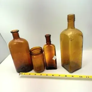 Collection of four antique amber glass bottles and jars in various shapes and sizes, shown with a measuring tape for scale.