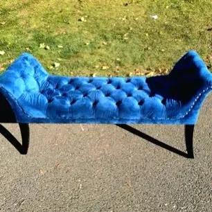 Vibrant royal blue velvet tufted bench with flared armrests and dark wooden legs.