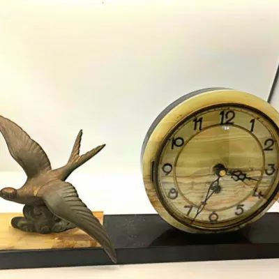 Art Deco onyx and metal mantle clock featuring a detailed bird figurine in flight alongside a round face on a rectangular base.