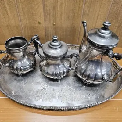 Vintage silver-plated tea and coffee service with a teapot, covered sugar bowl, and creamer set on an etched oval tray.