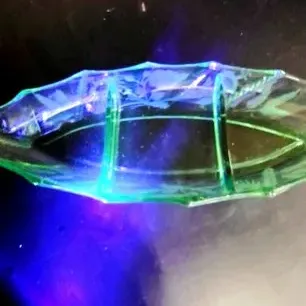 Vintage green uranium glass divided relish dish with etched floral patterns, glowing under a UV light.