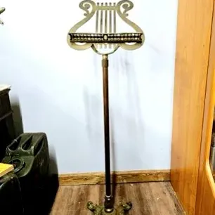 Vintage ornamental brass sheet music stand featuring a lyre motif design and an ornate four-legged base.