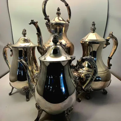 Four-piece ornate silver-plated tea and coffee service, featuring elaborate handles, spouts, and footed bases in a classic vintage style.