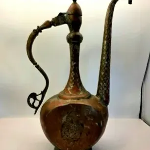 Antique Middle Eastern or Persian brass and copper aftaba ewer featuring an elongated spout, ornate handle, and decorative etched details.