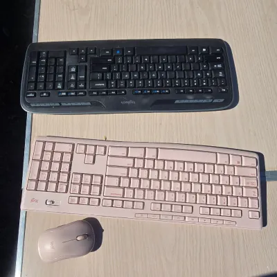 Sale Photo Thumbnail #149: Lot includes two Logitech computer keyboards (one black, one light pink/rose) and a matching pink Logitech wireless mouse. Items appear to be in good, pre-owned condition with light cosmetic surface wear. Functionality is unverified.