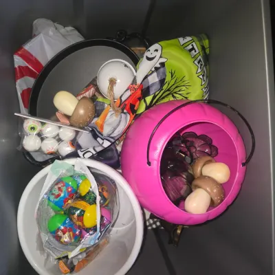 Sale Photo Thumbnail #131: A collection of holiday decor and trick-or-treat accessories contained in a grey storage tote. Includes a pink plastic pumpkin bucket, white plastic bucket, Easter egg hunt items, decorative mushrooms, novelty eyeball ping pong balls, felt bead garland, g