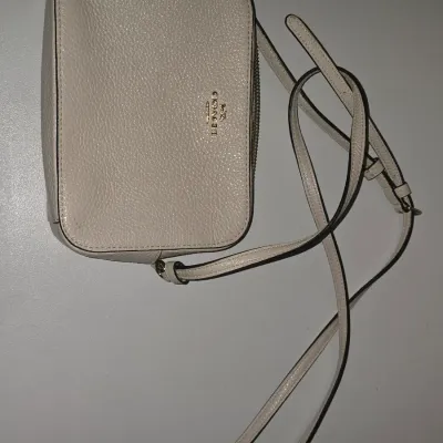 Sale Photo Thumbnail #94: small crossbody bag crafted in off-white/cream pebbled leather with gold-tone hardware. Features a top zip closure, and an adjustable shoulder strap. Pre-owned condition with slight surface wear visible along the edges and exterior.