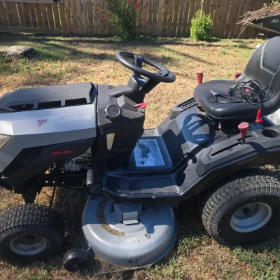 Sale Photo Thumbnail #107: Murray MT100 riding lawn tractor equipped with a 42-inch cutting deck. Shows typical outdoor cosmetic wear from use, including dirt accumulation on the deck and footrest areas, but appears complete. Black and metallic gray finish.