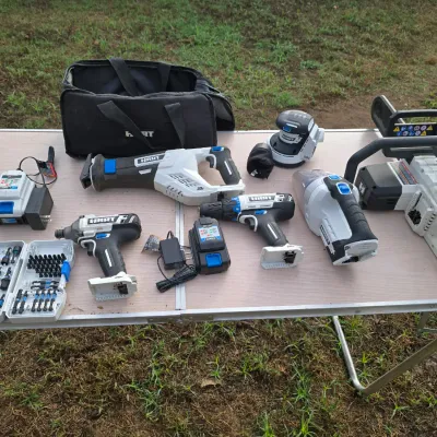 Sale Photo Thumbnail #159: Collection of HART 20V cordless power tools and accessories. Includes a mini chainsaw, reciprocating saw, drill/driver, impact driver, hand vacuum, random orbit sander, battery chargers, bit set, and a black HART soft tool bag. Items show light to moderat