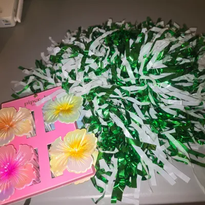 Sale Photo Thumbnail #71: Lot includes a set of four floral hibiscus-style hair claw clips by Piper Lou, mounted on original card packaging, along with a green metallic foil and white plastic cheerleading pom pom. Items appear unused/in good condition with no visible damage.