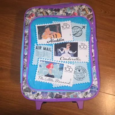Sale Photo Thumbnail #57: Includes a Disney 100 Years of Wonder rolling suitcase decorated with Princess postage stamp art (Aladdin, Cinderella, The Little Mermaid). Inside comes filled with various art and school supplies including Crayola limited edition character crayons, stand