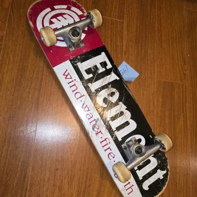 Sale Photo Thumbnail #189: Complete Element skateboard featuring classic 'Wind Water Fire Earth' deck graphics and Element logo. Fitted with metal trucks and white skate wheels. Shows signs of wear including scuffs, scratches on the deck bottom, and worn grip tape on top, consisten