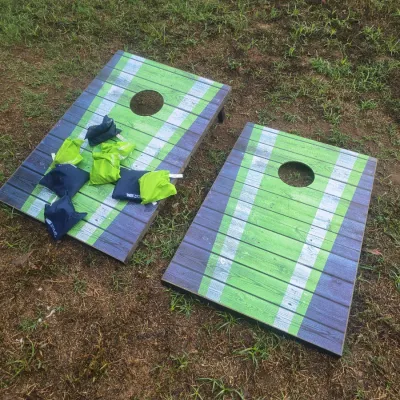 Sale Photo Thumbnail #152: Pair of wooden cornhole game boards featuring a green, blue, and white stripe finish. Includes two sets of bean bags (blue and green). Displays light wear from outdoor use but appears complete and functional.