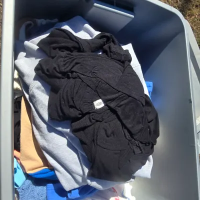 Sale Photo Thumbnail #111: An assortment of women's casual clothing stored in a plastic tub. Lot includes various shirts, knit sweaters, and tops including a tan 'Free Planet' graphic t-shirt, a pink short-sleeve knit sweater with a cherry print pattern, a tan and white patterned c