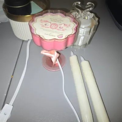 Sale Photo Thumbnail #75: Group of home accent items featuring a DW Home Sparkling Mimosa pink candle in a glass pedestal dish, two battery-operated flameless taper candles with cords, a glass candle with crystal swan figurines on the lid, and an additional white ceramic wax warme