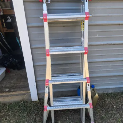 Sale Photo Thumbnail #137: Adjustable multi-position folding ladder made of aluminum with locking joints and red accents. Features multiple height settings and configurations. Shows light surface wear and scuffs consistent with use.