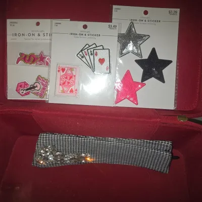 Sale Photo Thumbnail #50: Vintage red textured train case/jewelry box with handle and top carry latch, showing moderate surface wear and dust. Interior includes three packages of new iron-on embroidered patches (playing cards, stars, lettering) and a houndstooth fabric headband wi