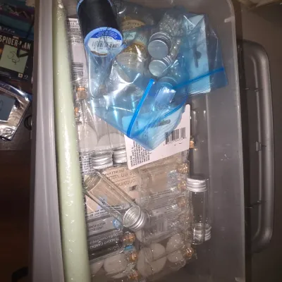 Sale Photo Thumbnail #73: Clear plastic storage tub containing various crafting and DIY supplies. Includes multiple small glass bottles/vials with screw caps and cork stoppers,  a long taper candle, thread, and accent beads/embellishments. Items appear to be new or unused in origi